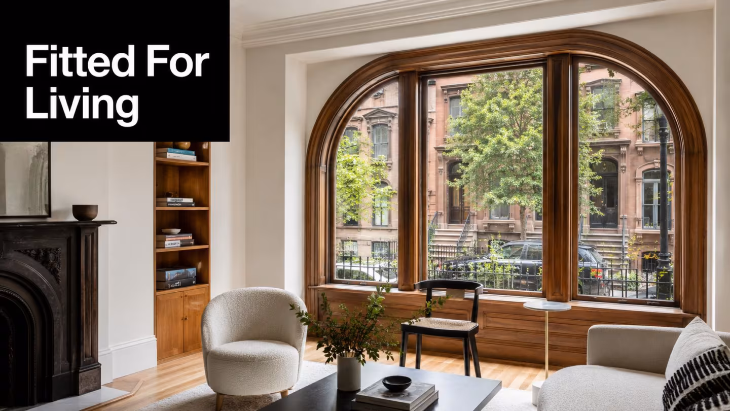A cozy, sunlit living room featuring a grand arched wooden window looking out onto a residential street.
